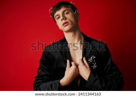 full length of young man with flowers in hair looking at camera and standing on red background