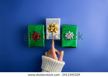 First person top view photo of female hands holding three shiny green and silver gift boxes with  bow on isolated  blue background
