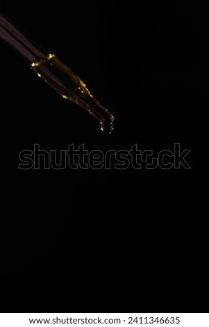 Glass pipette for cosmetics. A drop of cosmetics oil on a black background close-up macro