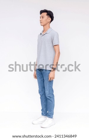A slim young asian man wearing a gray shirt and jeans. 45 degree angle. Full body photo isolated on a white background. Royalty-Free Stock Photo #2411346849