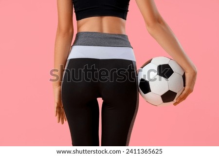 Beautiful young sporty woman with soccer ball on pink background, back view