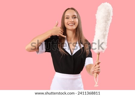 Young chambermaid with pp-duster showing "call me" gesture on pink background