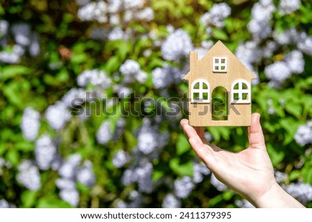 The girl holds in her hand the symbol of the house against the background of blooming lilac
