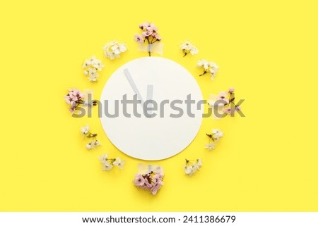 Clock made of paper and blooming branches on yellow background Royalty-Free Stock Photo #2411386679
