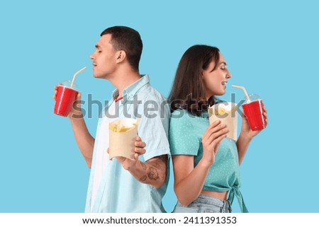 Young couple drinking cola and eating french fries on blue background