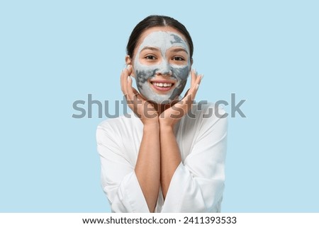 Young woman with clay mask on her face against blue background
