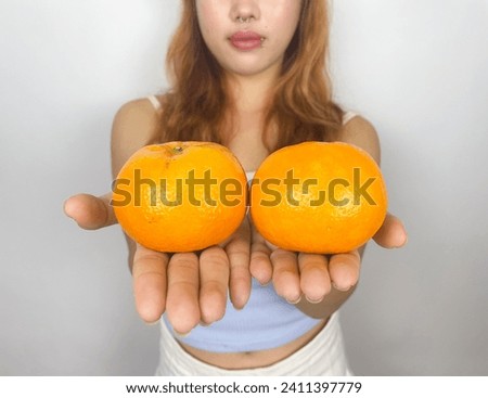 Beautiful, cute, teenage girl Standing for a photo in the studio holding an orange and a glass of orange, coloring your hair in a fashionable way. Smile happily and be excited and bright.