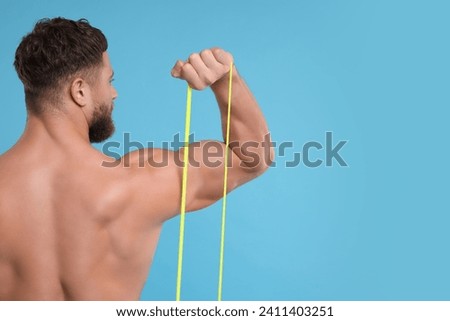 Young man exercising with elastic resistance band on light blue background, back view. Space for text
