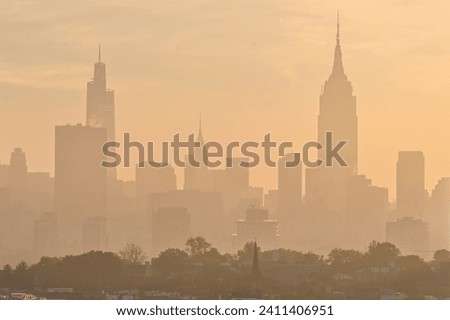 Horizontal photo of silhouetted midtown New York City skyline in a yellow haze with Hoboken in the foreground 