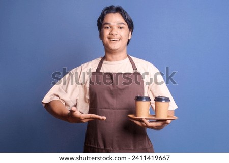 Cheerful young barista wear apron presenting two paper coffee cups on wooden tray 