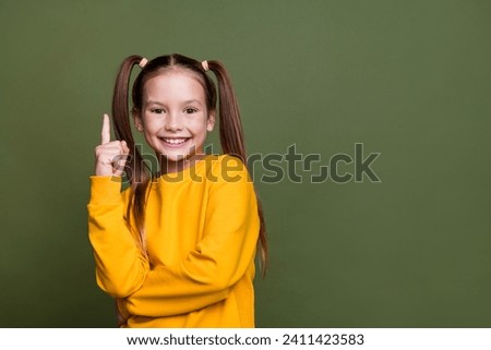 Portrait of smart clever small kid with tails dressed yellow sweatshirt raising finer up has idea isolated on khaki color background