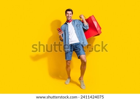 Full body photo of optimistic man dressed denim shirt shorts order new outfit in eshop smartphone app isolated on yellow color background