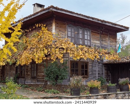 Old traditional Bulgarian house with wooden walls and windows and autumn leaves. Typical architecture from the Bulgarian National Revival period. Exterior greenery decoration. Historical place, Medven Royalty-Free Stock Photo #2411440939