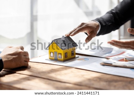 Real estate agents offer contracts to buy or rent housing. Businessman holding model small building house with property insurance at table in home sales office
