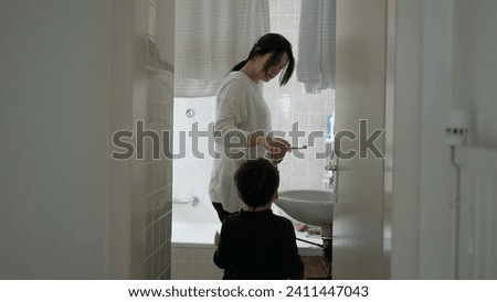 Candid mother and child standing in bathroom preparing to brush teeth together, domestic everyday lifestyle family activity, dental routine hygiene at home Royalty-Free Stock Photo #2411447043