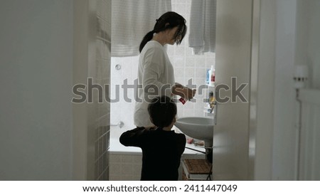 Candid mother and child standing in bathroom preparing to brush teeth together, domestic everyday lifestyle family activity, dental routine hygiene at home Royalty-Free Stock Photo #2411447049