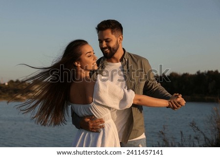 Beautiful couple dancing near river at sunset Royalty-Free Stock Photo #2411457141