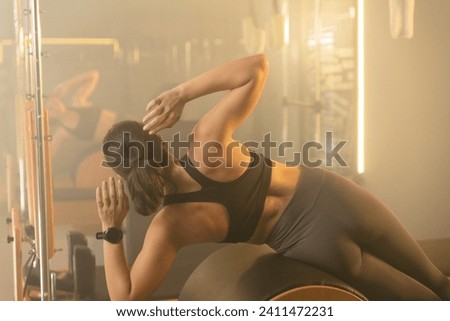 Photo of a young woman doing core exercises on a Reformer Pilates machine in a gym, focusing on her core strength