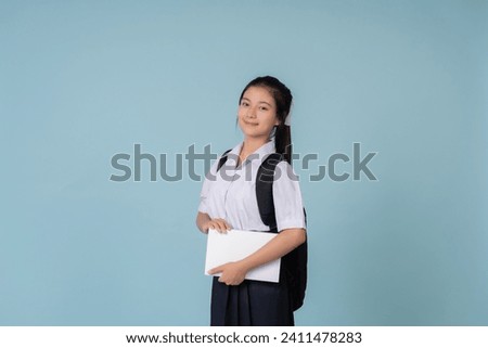Presenter for Asian female high school students in education Carrying a bag and a white textbook Use on websites or posters of tutoring institutions. Taking photos in a studio with a blue background