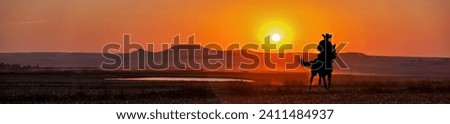 silhouette cowboy in the sunset riding near a water hole in the prairie, american western landscape vista Royalty-Free Stock Photo #2411484937