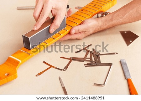 Guitar repairman aligns the frets on electric guitar neck with leveling bar. Royalty-Free Stock Photo #2411488951
