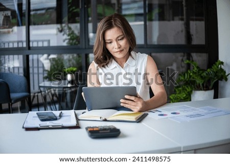 Businesswoman sitting at desk on couch in workplace or at home working on laptop and analyzing data on charts and graphs and writing on papers to make business plan and strategies for company, startup