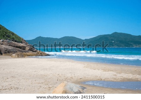 The picture shows a hidden, small sandy beach between rocks in a small bay on the mountainous slopes of an island covered in dense rainforest. Ilha de Santa Catarina, Brazil
