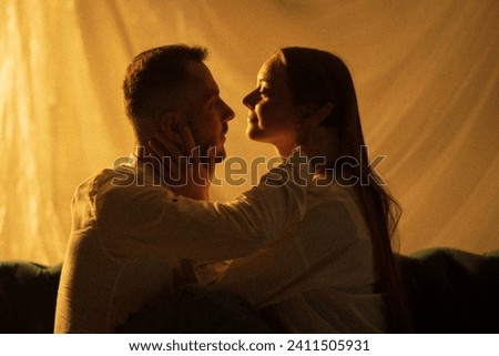Two lovers kissing on neon light background. Woman touching face her boyfriend when kisses indoors. Nightclub strangers hugging and seducing each other. Foreplay in relationship Royalty-Free Stock Photo #2411505931