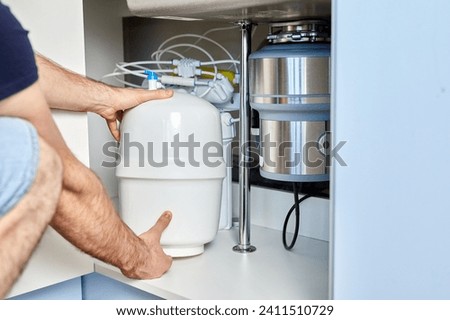 A plumber installs reverse osmosis equipment under the sink. The master installs a water filter in the kitchen. Installation of the cleaning system. Royalty-Free Stock Photo #2411510729