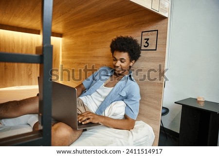 happy and stylish african american student networking on laptop on double-decker bed in hostel Royalty-Free Stock Photo #2411514917