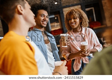 cheerful multicultural buddies with paper cups talking in lobby of hostel, travel and friendship Royalty-Free Stock Photo #2411515829