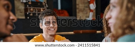 young stylish man smiling near multicultural buddies talking in lobby of students hostel, banner Royalty-Free Stock Photo #2411515841
