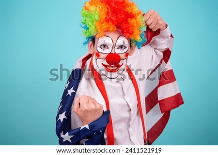 A funny clown with colored hair wrapped himself in the flag of America. Blue background. Celebration and fun. Work in the entertainment industry.