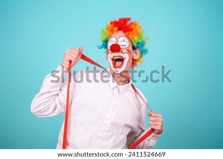 A joyful clown. A cute man in a suit and makeup for a holiday for children. A fool. Blue background. Copy the space.