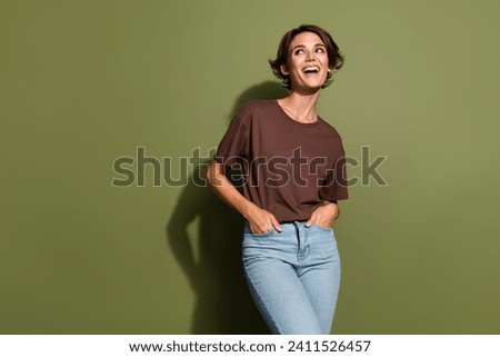 Portrait of cute girl with short hair wear oversize t-shirt arms in pockets look at offer empty space isolated on green color background