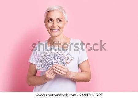 Photo portrait of pretty retired female hold banknotes fan look empty space dressed stylish white outfit isolated on pink color background