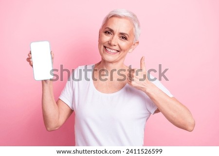 Photo of senior woman with short hair wear white t-shirt presenting eshop on smartphone screen show thumb up isolated on pink background