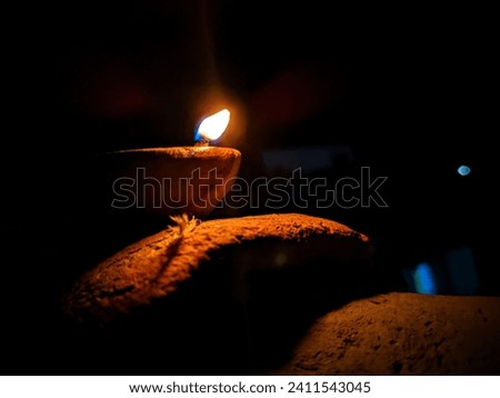 In the dark night, the clay oil lamp casts a soft, warm glow, creating an intimate ambiance. The flickering flame dances within, casting shadows that play on the surrounding surfaces. Royalty-Free Stock Photo #2411543045