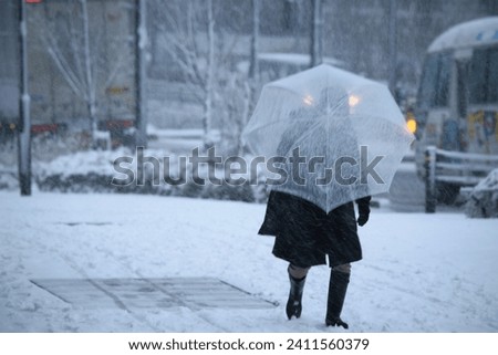 Person walking with a transparent umbrella on a snowy day. Royalty-Free Stock Photo #2411560379