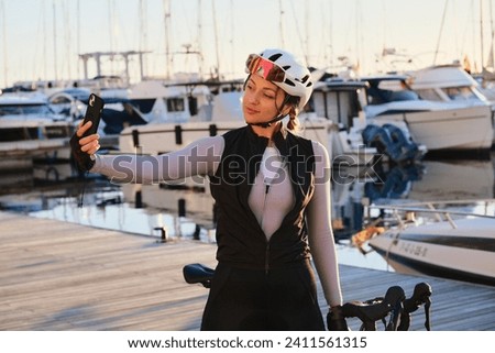 Beautiful fit woman cyclist taking a selfie with a mobile phone during training. Woman cyclist wearing cycling kit and white helmet riding a e-bike. Sports motivation image. Calp,Alicante,Spain.