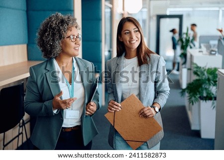 Happy mature businesswoman and her female coworker communicating while going through the office.