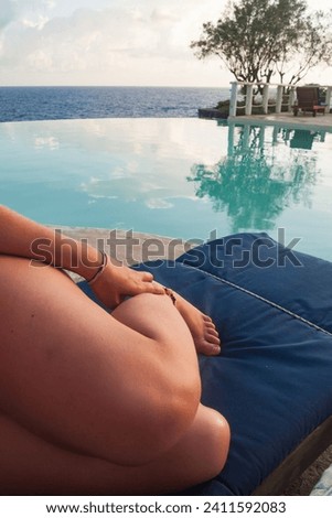 Girl with pretty legs and feet rests on a sun lounger above the infinity pool