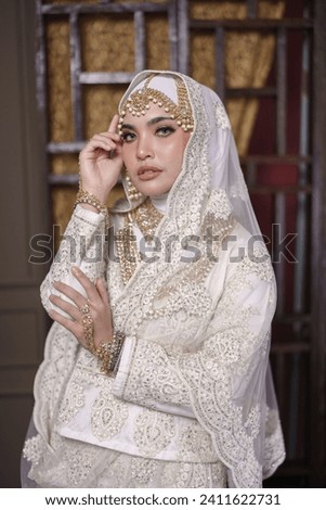 Beautiful Asian hijab girl wearing white traditional Bollywood India costume with jewelry set isolated over classic wall design background. Deepavali celebration and Bollywood concept.