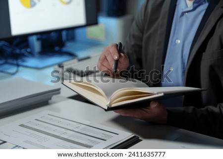 Young Asian businessman holds a pen to take notes in a notebook to plan his financial work. Balance sheet, net profit, taxes in a meeting on sales strategy topic. Presentation of work by the company.