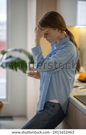 Tired exhausted woman feeling headache holding head with closed eyes on kitchen at home. Stressed girl suffers pain, migraine, cephalalgia, premenstrual syndrome taking medications, painkillers Royalty-Free Stock Photo #2411652463