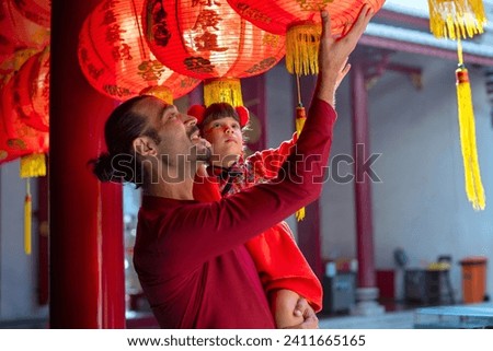 Happy father and daughter in traditional Chinese costumes enjoying a tour of the red lanterns in the shrine, Chinese New Year holiday, Chinese Letters mean wishing great wealth