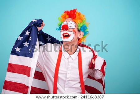 A funny clown with colored hair wrapped himself in the flag of America. Blue background. Celebration and fun. Work in the entertainment industry.