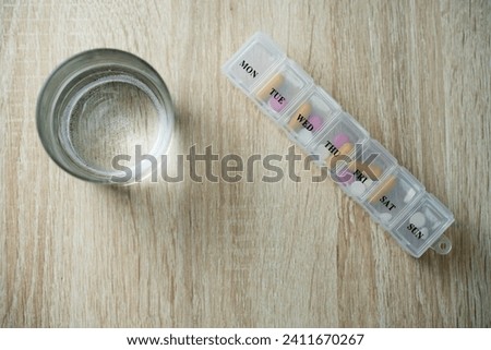 Pill box with pills and capsule vitamins and glass of water on a table background with copy space, top view. Medical pill box with daily doses of medication Royalty-Free Stock Photo #2411670267