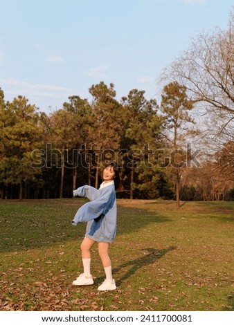 Beautiful young Chinese woman dancing with joy in sunny summer forest, wearing blue loose oversized top, mini skirt and white shoes. Emotions, people, beauty, youth and lifestyle portrait.