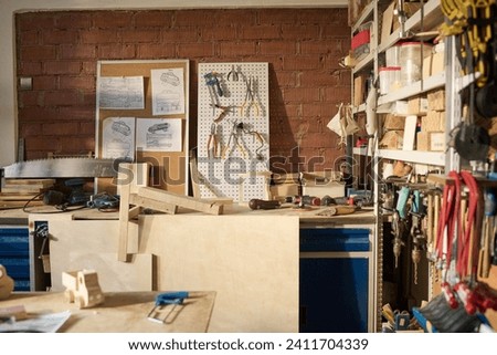 Wide angle view at carpentry workshop in sunlight with various tools and wooden models on table Royalty-Free Stock Photo #2411704339